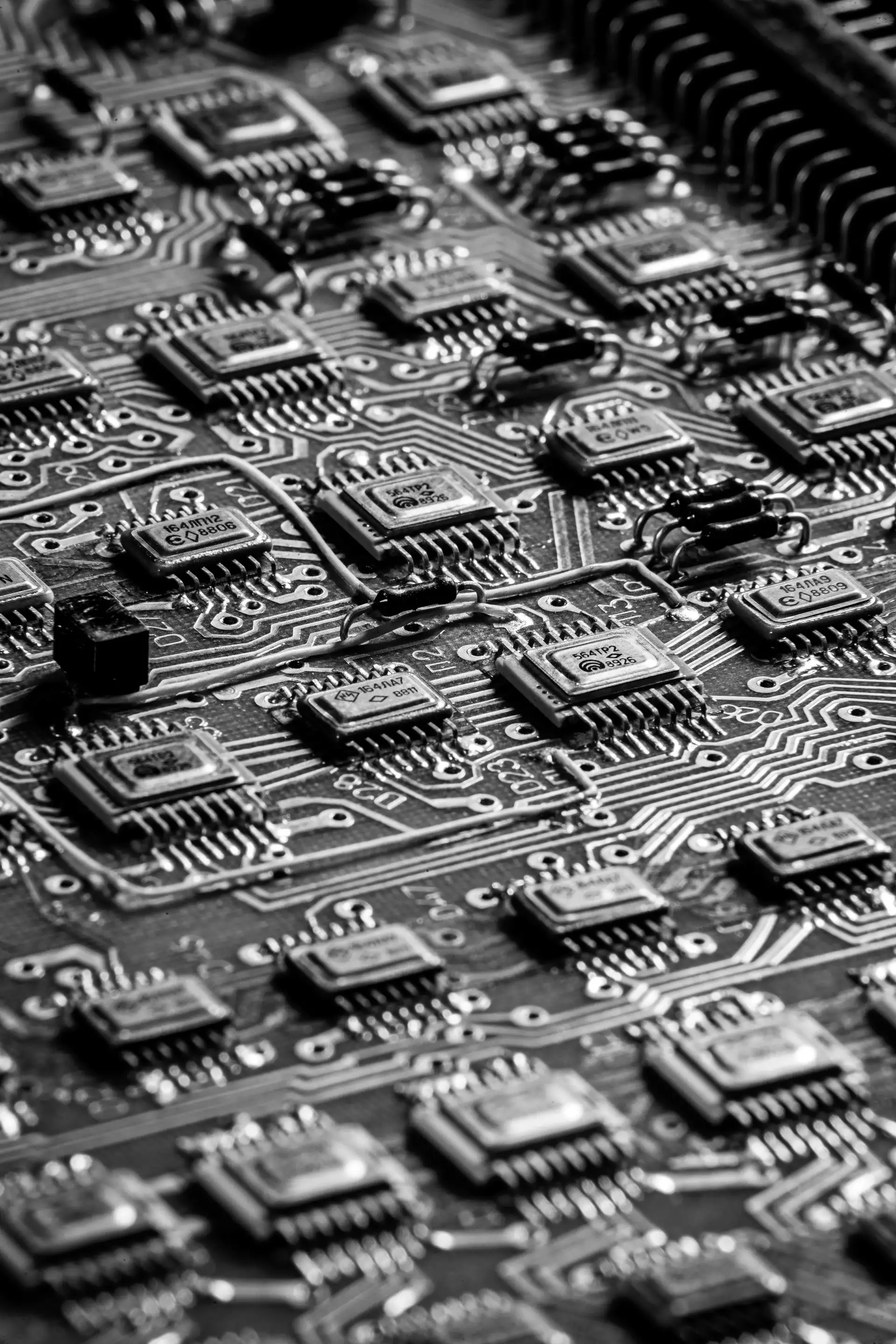 Black and white macro of a densely populated logic board, rows of surface-mount chips and hand-soldered jumper wires receding under shallow depth of field.